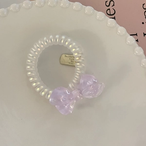 Close-up of spiral hair tie with a lavender resin bow and golden metal identity tag