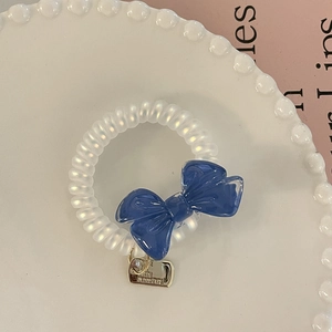 Detail of white spiral hair tie with blue bow and gold metal pendant on plate