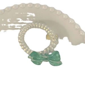 White spiral telephone wire hair tie with a mint green bow on a minimal stand