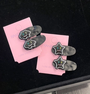 Close-up of matte black hair clips with smiley cloud and star designs on pink card