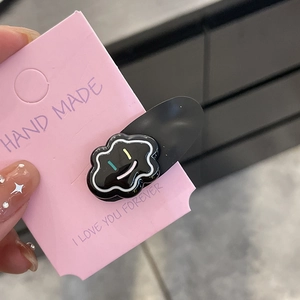 Detail view of handmade black cloud hair clip with colorful smiley faces on pink card