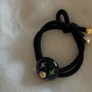 Détail d'un élastique à cheveux noir avec perle à motifs et embouts dorés