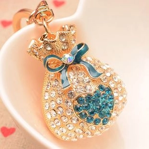 Detail showing a golden money bag charm with crystal hearts and blue bow for bags