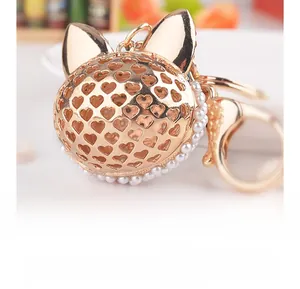 Détail macro du porte-clés chat doré avec motifs de cœur évidés et perles blanches