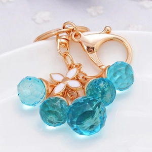 Detail of gold keychain with blue crystals and a white enamel flower charm decoration