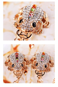 Macro detail of golden toad keychain with colorful rhinestones on marble background