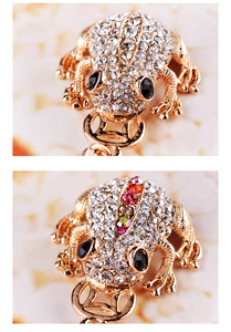 Macro detail of two golden toad keychains with sparkling crystals and coin accents
