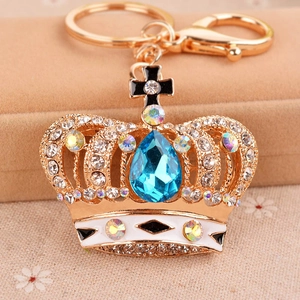 Elegant gold crown keychain with blue crystal and white rhinestones on a beige background