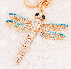 Macro detail of golden dragonfly keychain with blue rhinestones and intricate cutout wings