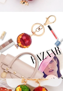 Cute pomegranate fruit keychain with red enamel and gold clasp beside a handbag