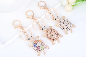 Close-up of three gold turtle keychains with sparkling rhinestones and lobster clasp