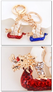 Detail of dragon boat keychain with enamel finish and rhinestones on beige fabric