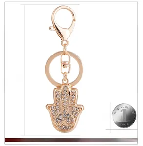 Détail d'un porte-clés main de Fatma dorée avec strass et comparaison de taille réelle