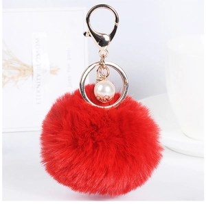Detailed macro view of bright red faux fur pompom keychain with elegant pearl charm and gold clip