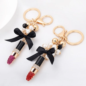Porte-clés rouge à lèvres avec perles et nœuds en tissu sur un fermoir doré brillant