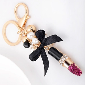 Porte-clés rouge à lèvres doré avec nœud noir et strass roses sur fond blanc pur