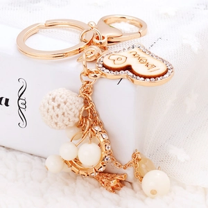 Portachiavi dorato con cuore in legno, perle e palla di maglia su sfondo bianco romantico