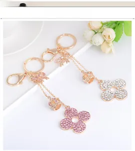 Detailed macro view of gold-plated pink and white crystal clover keychains in a white tray