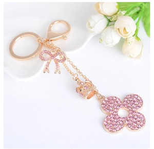 Close-up of sparkling pink rhinestone bow, crown, and clover keychain on gold hardware