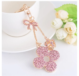 Close-up of pink rhinestone flower keychain with crown and bow charms on rose gold metal