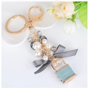 Détail d'un porte-clés avec perles blanches, nœud en soie grise et mini sac à main bleu