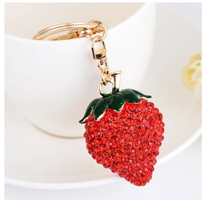 Detailed view of rhinestone strawberry keychain with gold lobster clasp on white cup