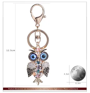 Detailed size comparison of golden owl keychain with rhinestones against a coin