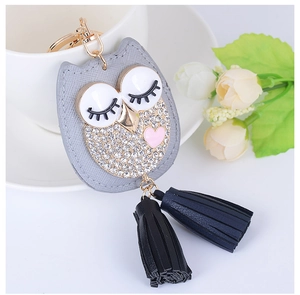 Détail du porte-clés chouette en cuir avec strass et pompon posé sur une tasse