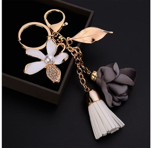 Detailed view of floral keychain featuring white enamel flower, leaf, and silk blossom