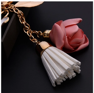 Macro view of a gold chain keychain with pink silk rose and elegant white tassel
