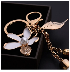 Macro shot of white enamel flower keychain with pearl and gold leaf in a gift box