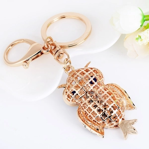 Golden owl keychain with blue crystal eyes and hollow pattern on white ceramic plate