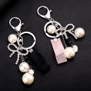 Fashionable pearl keychain with rhinestone bow and heart charm on black leather background