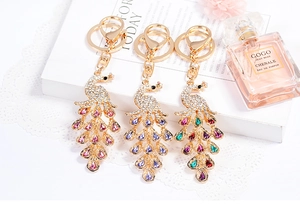 Peacock crystal keychains in pink and purple colors on a white book with a perfume bottle