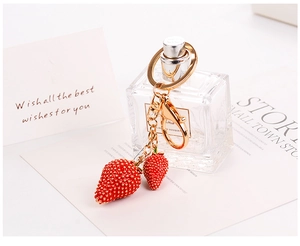 Dettaglio del portachiavi a fragola in lega con anello dorato su sfondo estetico e pulito