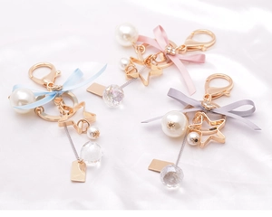 Close-up of star pearl bow keychains with crystal ball on white silk fabric background