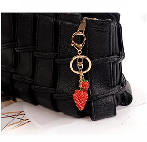 Dettaglio macro del portachiavi con fragola rossa appeso a una borsa in pelle intrecciata