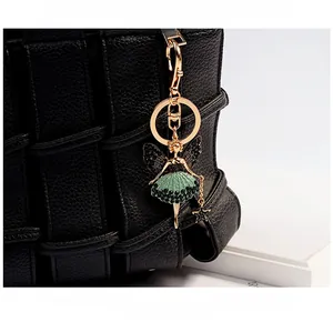 Detailed view of a gold ballerina pendant with green rhinestones on a black woven bag