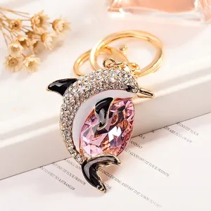 Golden dolphin keychain with pink crystal and sparkling white zircons on a white pedestal