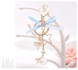 Detail of blue silk bow keychain with gold star and pearls on white jewelry stand
