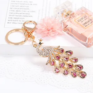 Golden peacock keychain with pink and white crystals shown on a stylish magazine background