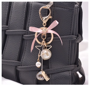 Detail of pink silk bow keychain with pearls and crystal on black woven leather bag