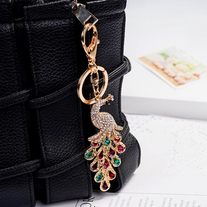 Sparkling crystal peacock keychain with colorful gemstones hanging on a black leather bag