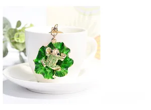 Detail of green enamel frog on lily pad keychain hanging on a white ceramic cup