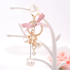 Pink ribbon bow keychain with golden star, clover and pearl charms on jewelry stand