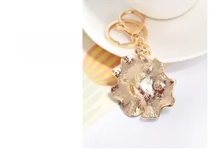 Detail of a golden alloy flower keychain featuring a polished textured finish and clasp