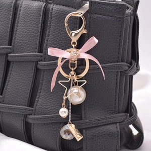 Pink bow keychain with pearls and clover charm on a black woven texture handbag