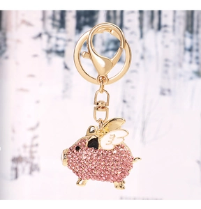 Close-up of golden flying pig keychain with pink crystals and white wings detail