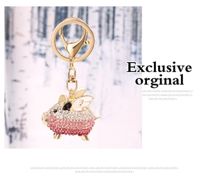 Detailed close-up of a golden flying pig keychain with pink rhinestones and wings