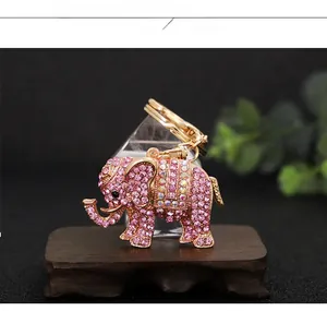 Detail view of pink rhinestone elephant keychain on dark wood tray with prism reflections
